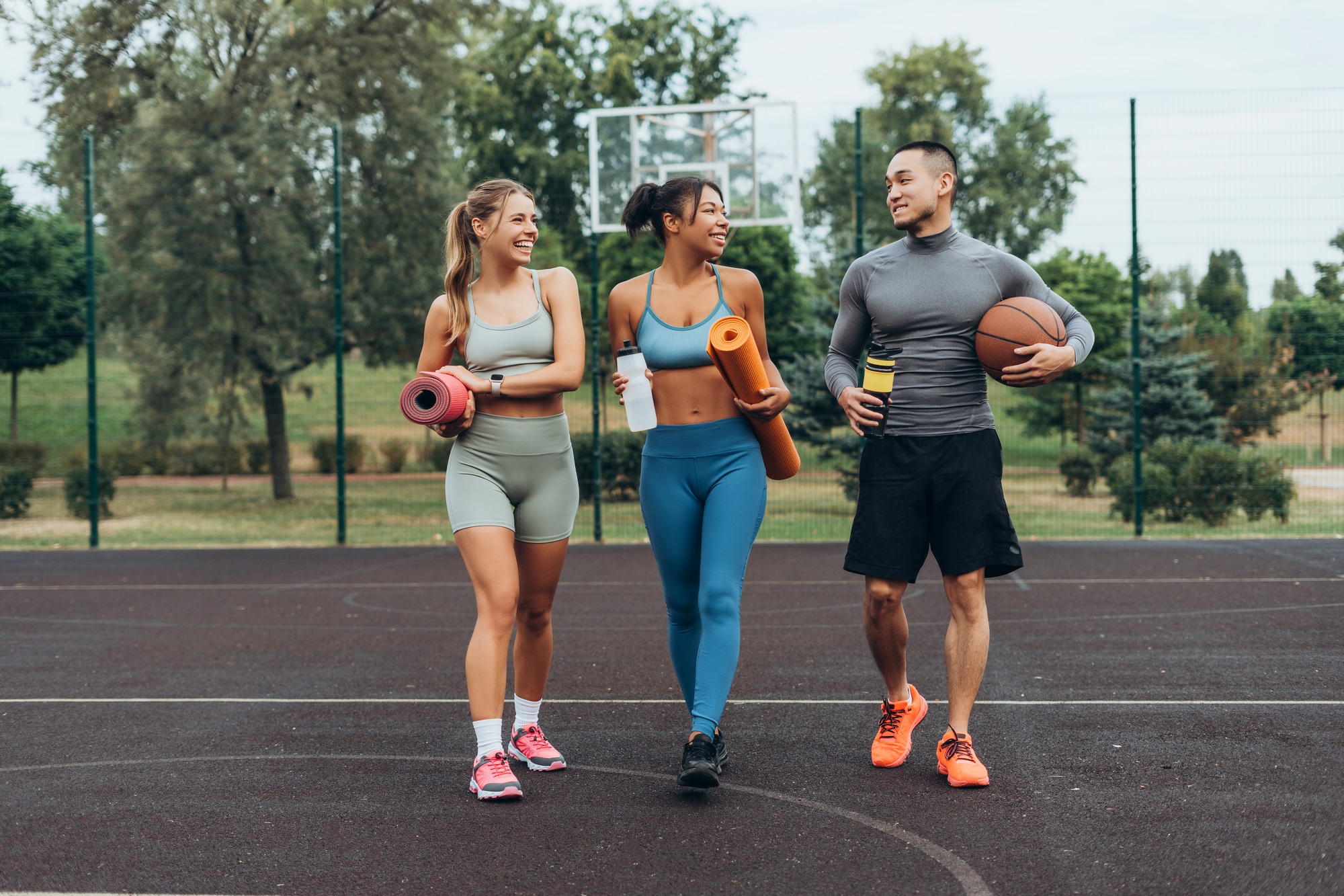 Active, multinational group of friends walking, training together on the street holding sport mat
