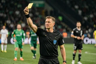 Arbitre UEFA en tenue officielle brandissant un carton jaune lors d'un match de Ligue des champions